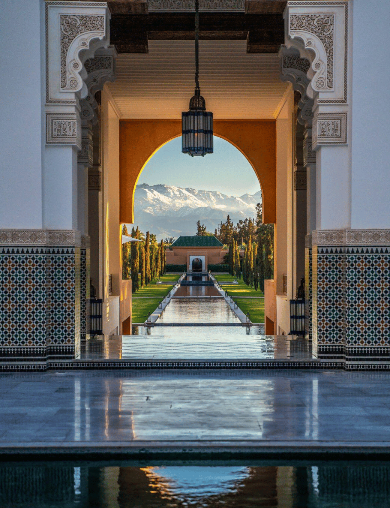 Snow-capped Atlas Mountains seen through a beautifully decorated Moroccan riad with a reflective pool in the foreground